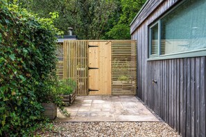 A wooden gate leading to a paved patio area with a wooden fence and a building with a window.