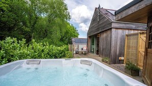 Een bubbelbad in een achtertuin, met een houten huis en een zonnepaneel op de achtergrond.