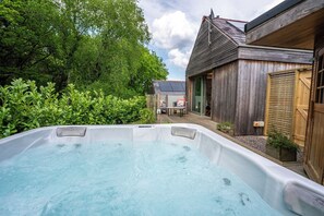 Ein Whirlpool in einem Garten mit einem Holzhaus und einer Solaranlage im Hintergrund.