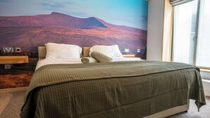 Een slaapkamer met een bed, kussens, een deken, een nachtkastje en een wanddecoratie.