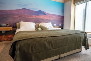 Ein Schlafzimmer mit einem Bett, Kissen, einer Decke, einem Nachttisch und einem Wandgemälde.