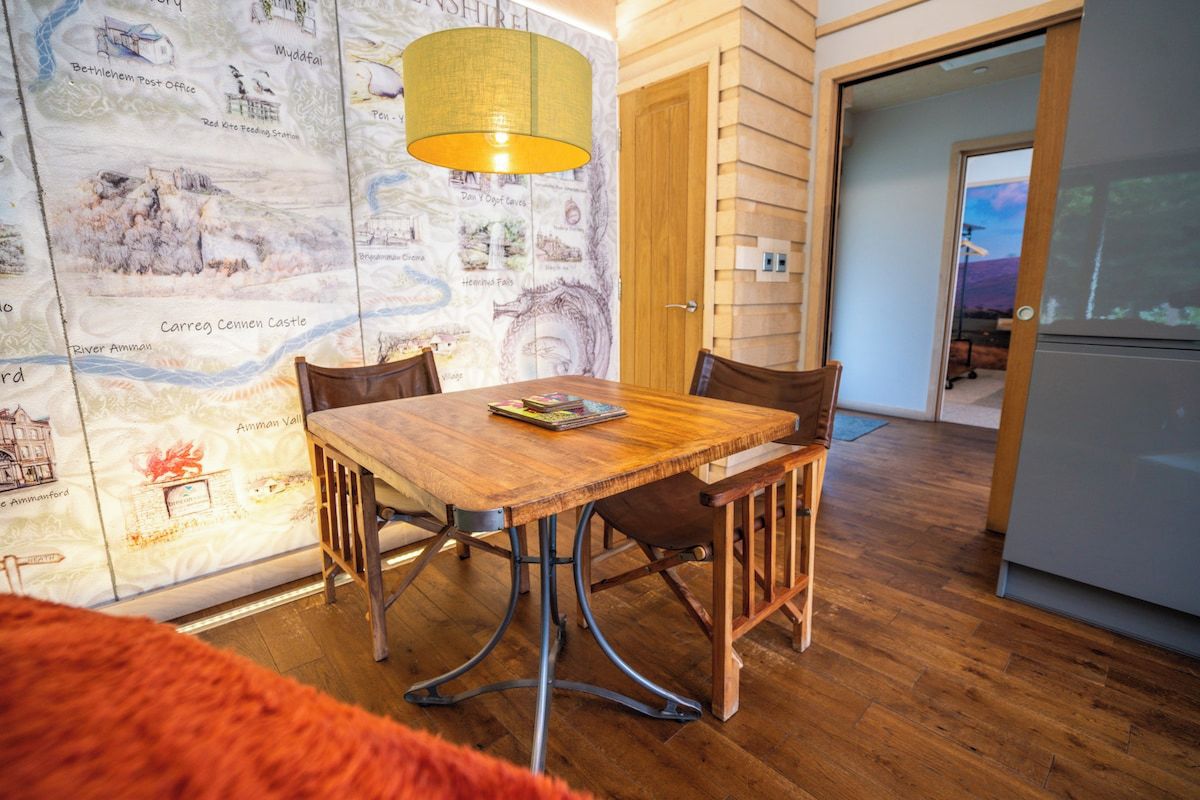 Un coin repas avec une table et des chaises en bois, un mur décoré d’une carte et une porte donnant sur une autre pièce.
