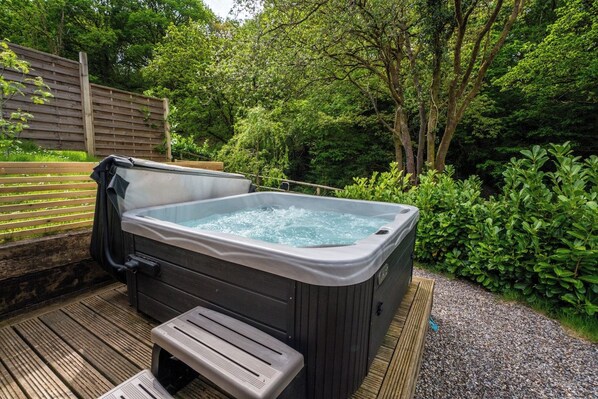 A hot tub on a wooden deck surrounded by lush greenery.