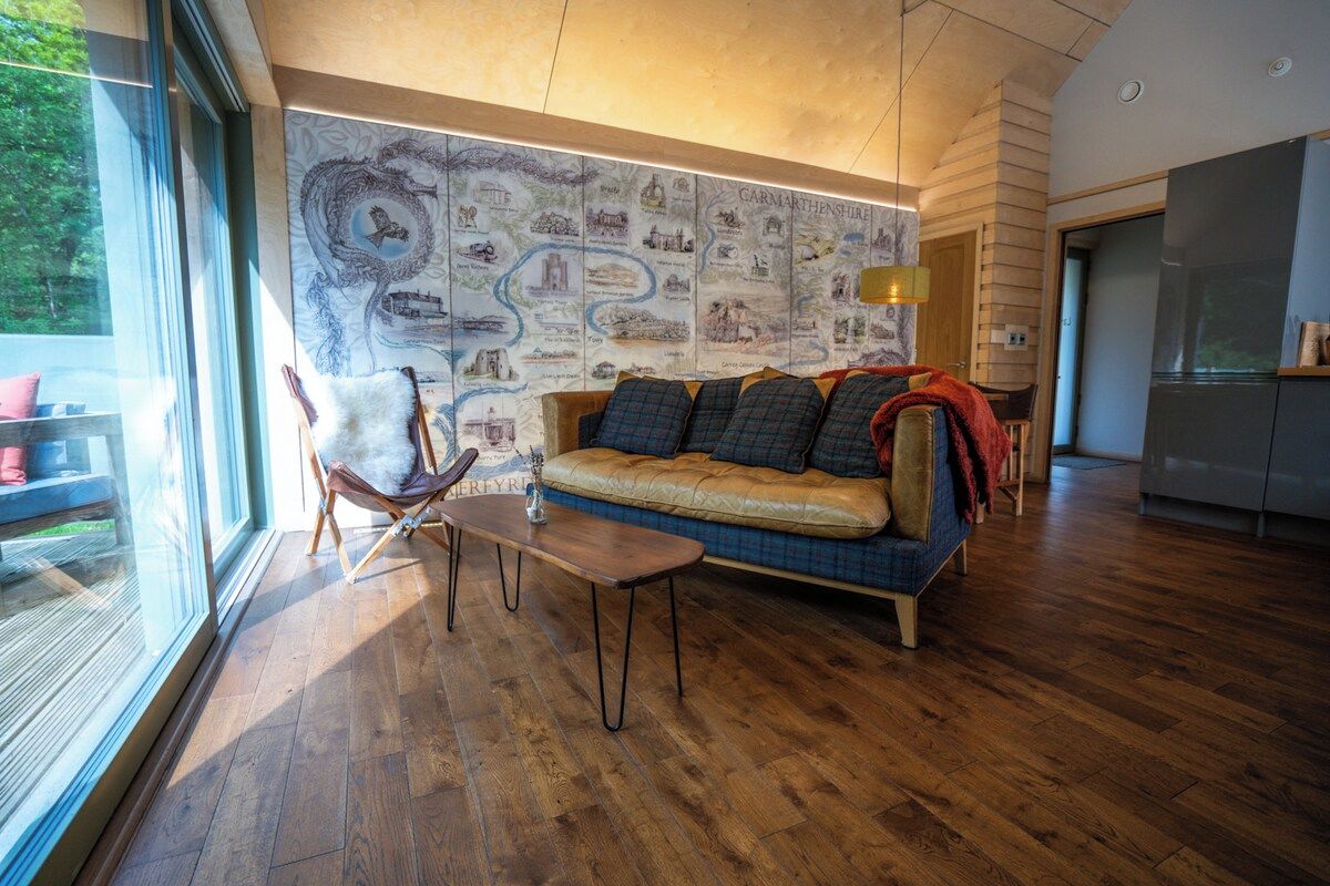 Una sala de estar moderna con piso de madera, un sofá con cojines estampados, una mesa de vidrio y una pared con un mapa.