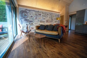 A modern living room with a wooden floor, a sofa with patterned cushions, a glass table, and a wall with a map.