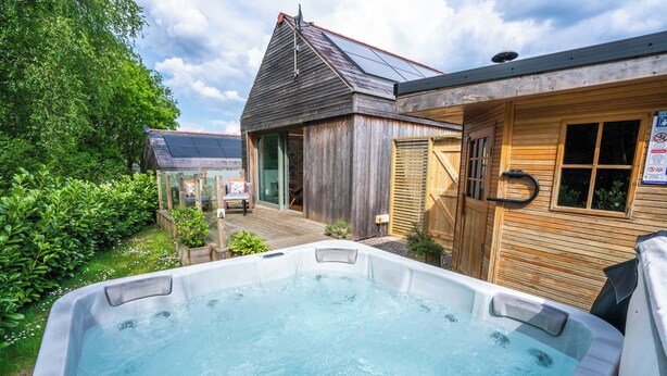 Een hottub in een tuin, met een houten gebouw op de achtergrond.