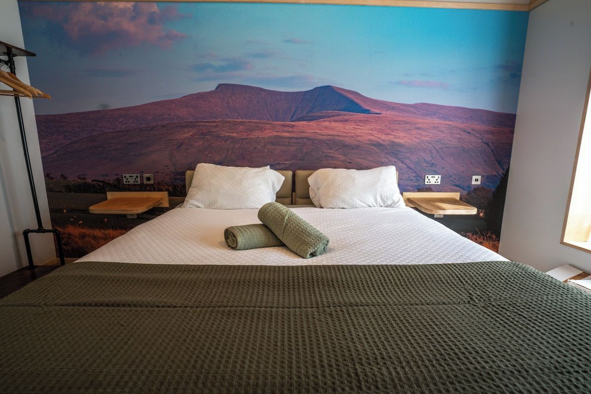 A hotel room with a large bed, two pillows, a rolled towel, and a view of a mountain landscape.