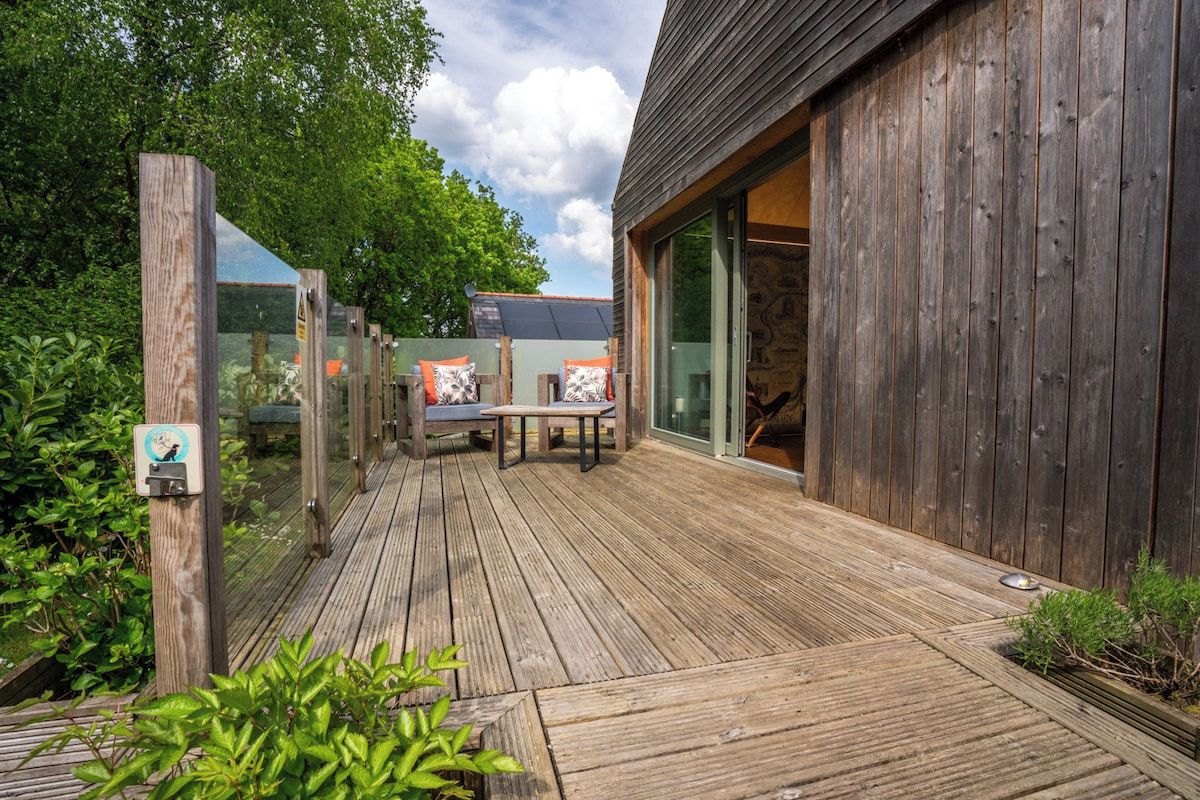 Una terraza de madera con mobiliario exterior y una puerta de vidrio que da a un edificio.