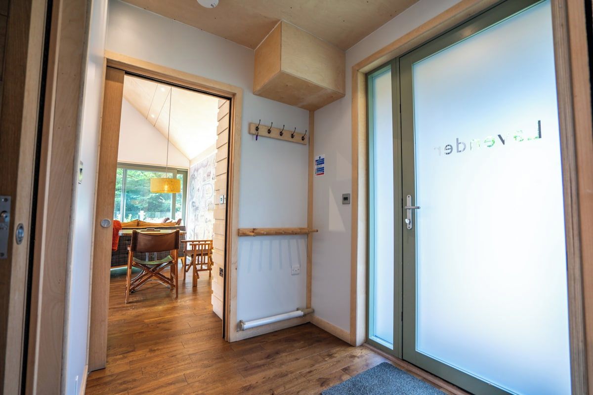 A hotel room with a wooden floor, a dining area with a table and chairs, a coat rack, and a door with frosted glass.