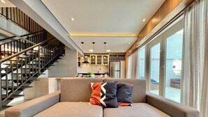 A modern living room with a sofa, a staircase, and a kitchen in the background. - Duplex Incrível, 2 Quartos, varanda, 2 vagas Batel (Curitiba)