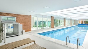 An indoor swimming pool with clear glass walls, a brick wall, and a modern ceiling design. - Duplex Incrível, 2 Quartos, varanda, 2 vagas Batel (Curitiba)