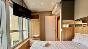 A hotel room with a bed, a wooden wardrobe, a small seating area with a cushion, and a sign indicating the availability of Netflix and Disney+ streaming services. - Duplex Incrível, 2 Quartos, varanda, 2 vagas Batel (Curitiba)