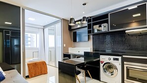 A modern kitchen with a washing machine, a dining area with a glass table, and a sofa.