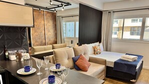 A modern hotel room with a dining area, a sofa bed, and a large window.