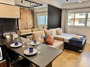 A modern hotel room with a dining area, a sofa bed, and a large window. - Studio reformado no Batel para 4, piscina aquecida e Shopping Curitiba em frente (Curitiba)