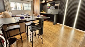 A modern kitchen with a dining area, wooden flooring, a flat-screen TV, and a built-in air conditioning unit.