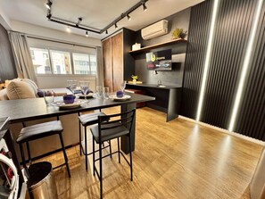 A modern kitchen with a dining area, wooden flooring, a flat-screen TV, and a built-in air conditioning unit. - Studio reformado no Batel para 4, piscina aquecida e Shopping Curitiba em frente (Curitiba)