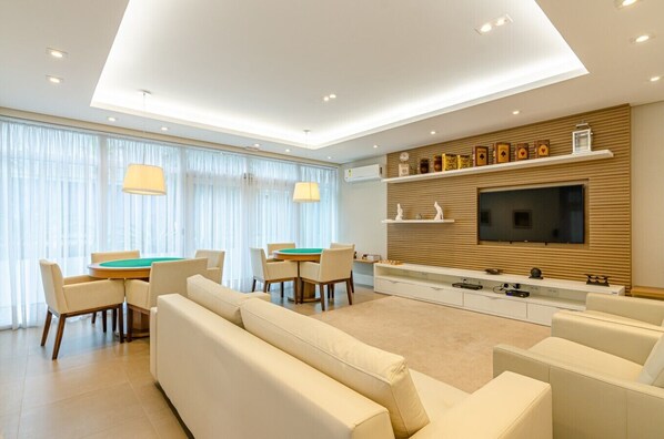 A modern living room with a pool table, sofas, a TV, and a wooden wall with shelves.