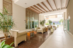 A modern lobby with wicker furniture, a wooden floor, and large windows. - Studio reformado no Batel para 4, piscina aquecida e Shopping Curitiba em frente (Curitiba)