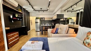 A modern hotel room with a flat-screen TV, a sofa, a bed, a desk, and a kitchenette.