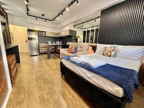 A modern bedroom with a large bed, a kitchenette in the background, and a wooden floor. - Studio reformado no Batel para 4, piscina aquecida e Shopping Curitiba em frente (Curitiba)