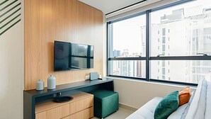 A modern living room with a large window, a flat-screen TV, a wooden cabinet, and a green ottoman.