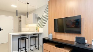 A modern kitchen with a built-in TV, bar stools, and a wooden accent wall.