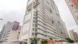 A tall, modern high-rise building with multiple balconies and a mix of white and beige exterior colors.