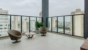 A spacious balcony with a high ceiling, two wicker chairs, a small table, and a potted plant. - Apto charmoso de 1 quarto mais sala ed. Elysia (Curitiba)