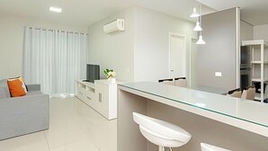 A modern kitchen with a glass island, white cabinetry, and pendant lighting. - Apartamento com Vista do 22º Andar, Piscina Aquecida e Garagem | Batel, Curitiba (Curitiba)