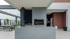 A modern outdoor kitchen area with a built-in grill, seating, and a view of the cityscape.
