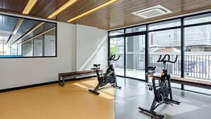 A gym with exercise bikes, a bench, and large windows offering a view of buildings outside.