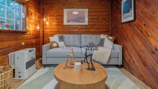 Un ambiente accogliente con un divano grigio, pareti in legno, un tavolino rotondo in legno e un quadro incorniciato appeso al muro.