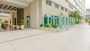 A modern hotel entrance with a glass door, potted plants, and a clean, tiled floor.