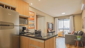 Eine moderne Küche mit Kühlschrank, Mikrowelle und Herd, ein Essbereich mit einer Couch und einem kleinen Tisch, sowie ein großes Fenster mit Vorhängen.