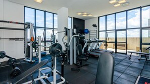 Ein Fitnessstudio mit unterschiedlichen Trainingsgeräten, großen Fenstern und Blick auf die Stadt.
