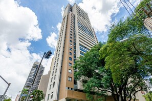 Un edificio alto con varios pisos, rodeado de árboles y otros edificios.