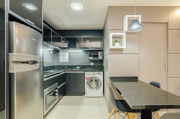 A modern kitchen with stainless steel appliances, a built-in washing machine, and a dining area with a table and chairs.