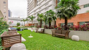 A well-maintained outdoor area with a grassy lawn, wooden benches, and potted plants. - 1 quarto elegante e sofisticado lifespace Curitiba (Curitiba)