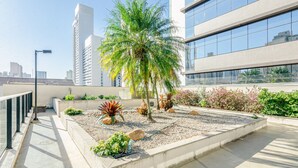 A rooftop garden with palm trees, various plants, and a concrete pathway. - Apto Completo com 1 quarto em frente shop estação. (Curitiba)