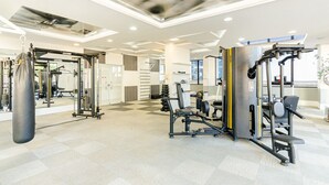 A modern gym with various exercise equipment, a punching bag, and a mirrored wall. - Apto Completo com 1 quarto em frente shop estação. (Curitiba)