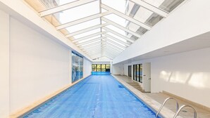 An indoor swimming pool with a skylight ceiling, clear glass doors, and a blue pool floor. - Apto Completo com 1 quarto em frente shop estação. (Curitiba)