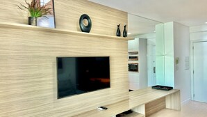 A modern living room with a flat-screen TV mounted on a wooden wall, a bench, and a small table with decorative items.