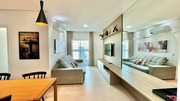 A modern living room with a sofa, a dining table, and a TV mounted on the wall.