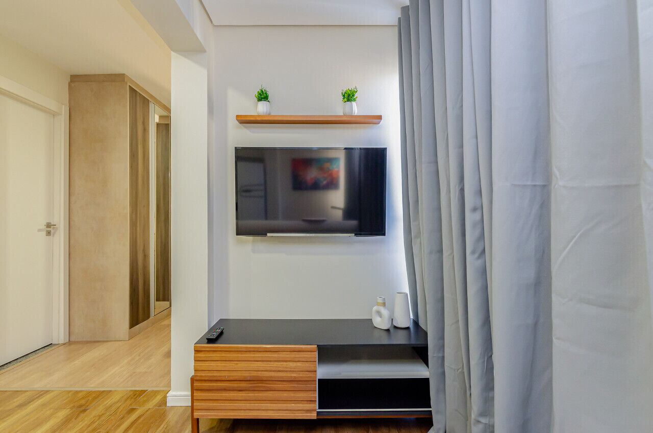A modern living room with a flat-screen TV mounted on the wall, a wooden entertainment unit below, and a small shelf with two potted plants.