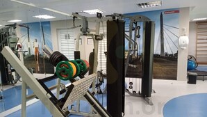 A gym with weightlifting equipment, a blue floor, and a wall with a bridge picture. - Studio 25º Andar Sacada e Linda Vista no Hydepark (Curitiba)