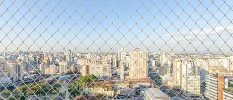 Vista de un paisaje urbano a través de una cerca de alambre, con una mezcla de edificios altos y estructuras más pequeñas.