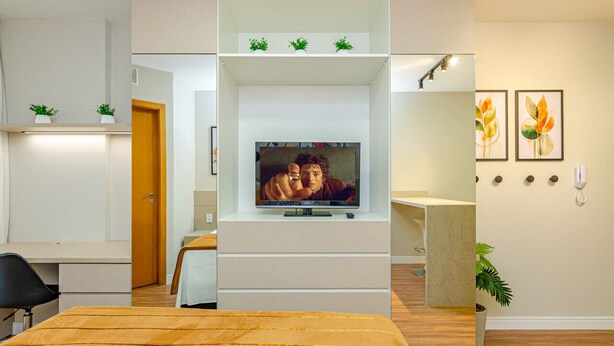 A modern hotel room with a TV on a white stand, a bed with a wooden headboard, a desk, and a chair. - Studio 25º Andar Sacada e Linda Vista no Hydepark (Curitiba)