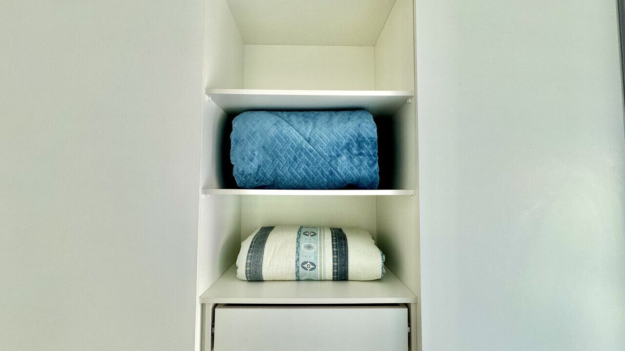 Een witte opbergunit met twee planken, waarvan er een een blauwe deken bevat en de andere een witte deken met blauw en zwart gestreept.