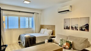 A hotel room with a bed, a sofa, a table, and a window with curtains. - Studio no lifespace Curitiba batel, com garagem (Curitiba)